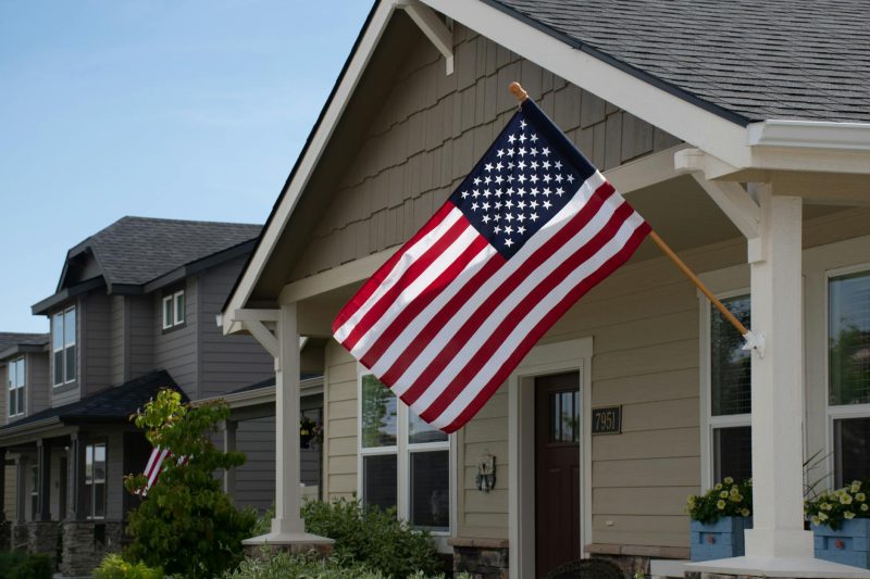 A vibrant American flag flutters outside a stylish suburban house on a sunny day.