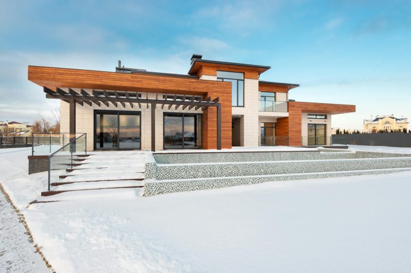 Contemporary suburban house with a terrace and large windows, surrounded by snow on a winter day.