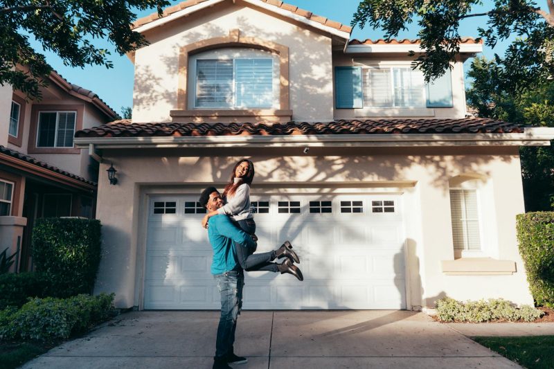 Joyful couple celebrating in front of a newly purchased house on a sunny day.