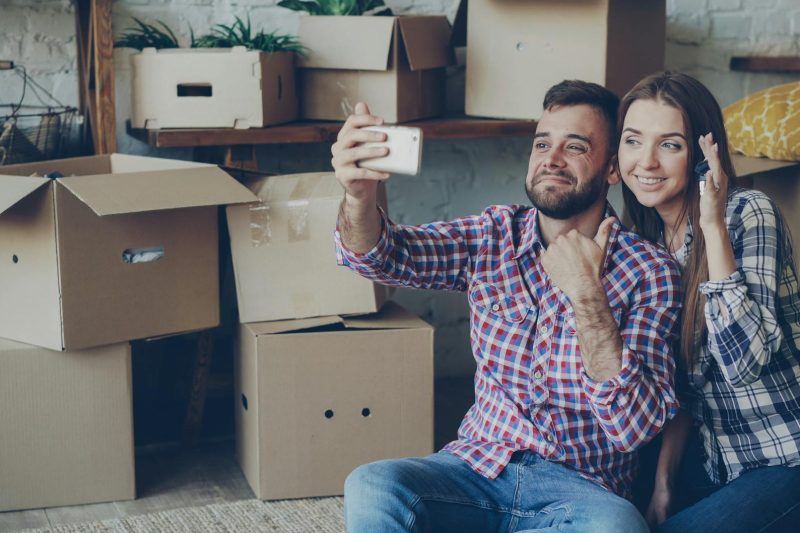 Happy couple smiling and taking a selfie among moving boxes in their new home.