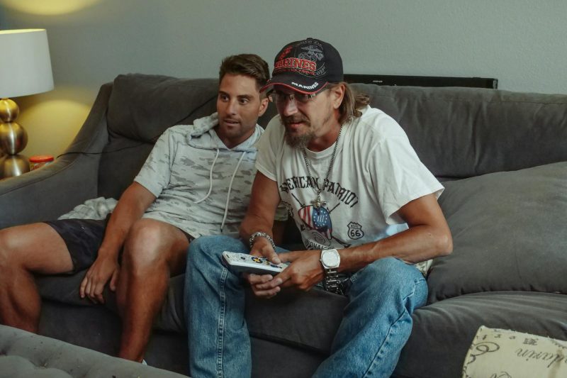 Two men relaxing on a couch, casually bonding while watching television in a cozy living room.