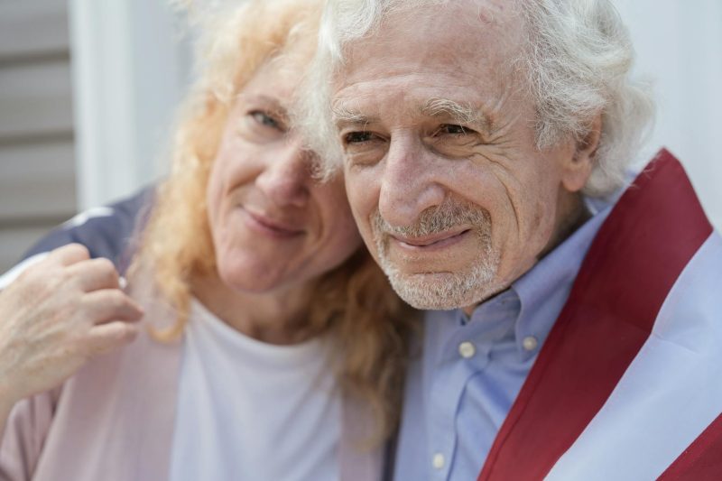 Senior couple wrapped in an American flag, smiling happily and symbolizing love and patriotism.