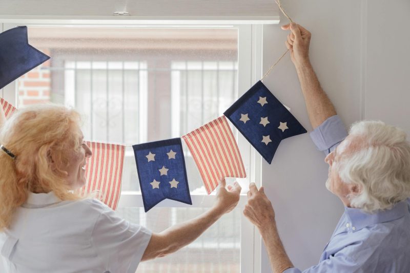 Elderly couple indoors decorating with patriotic banners for a festive 4th of July celebration.
