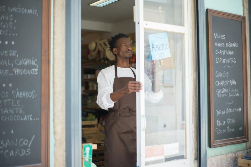 A man in an apron opens the door to a grocery store in Portugal, ready for business.