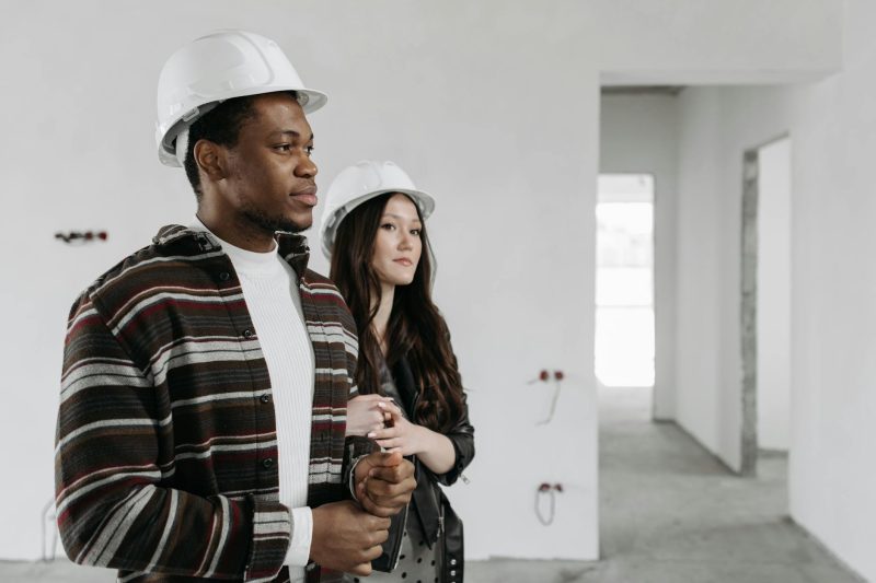 Interracial couple in hard hats examining the interior of a new house under construction.