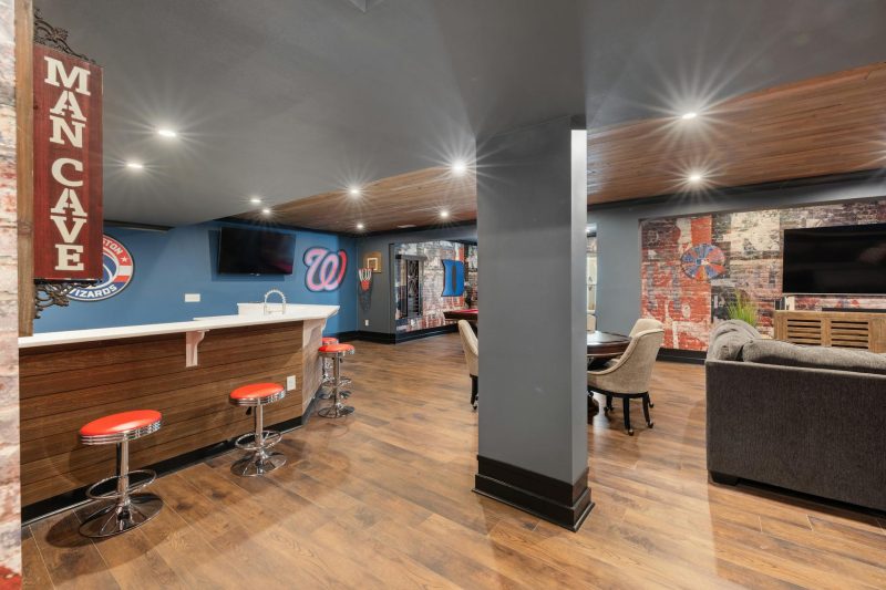 Sleek man cave featuring a bar, sports decor, and comfortable seating.