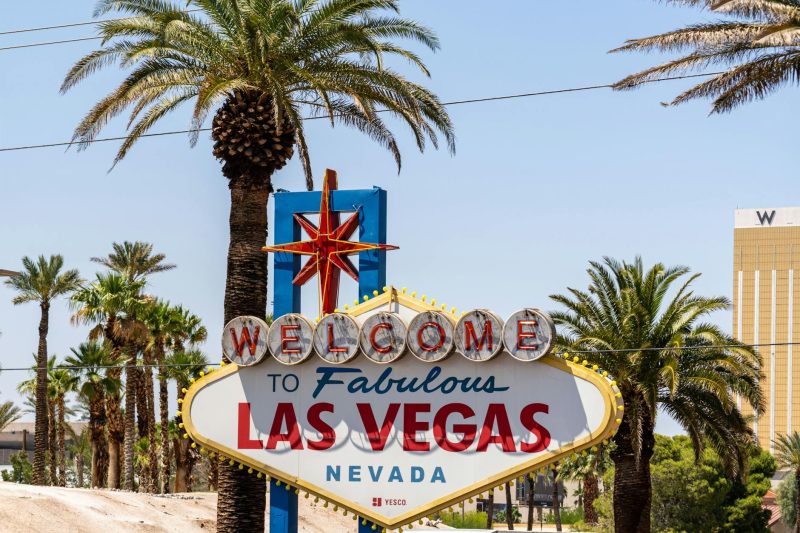 Classic 'Welcome to Las Vegas' sign surrounded by palm trees under a bright blue sky.