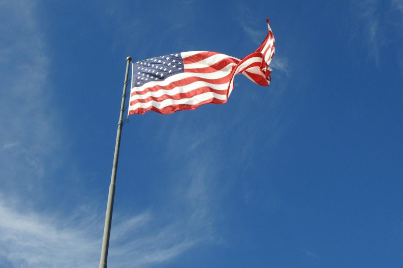 A vibrant American flag waves against a clear blue sky.