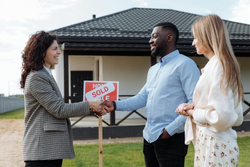 Real estate agent shaking hands with a diverse couple in front of their new home.