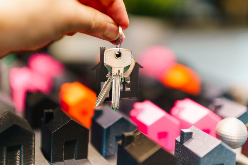 A hand holds keys above colorful miniature houses, symbolizing real estate choices and new beginnings.