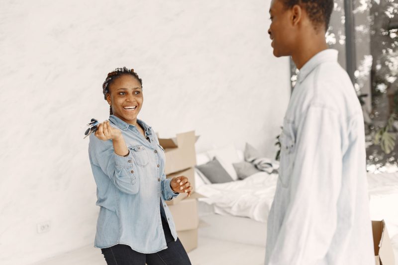 Smiling couple indoors, holding house keys, celebrating their move into a new home.