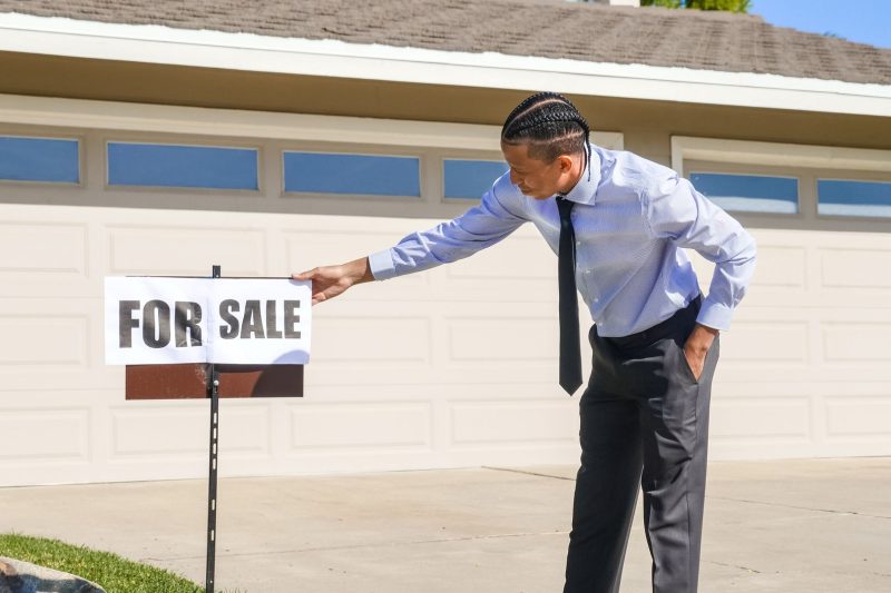 Professional real estate agent placing a for sale sign in front of a house.